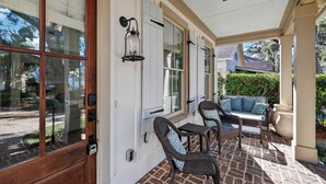 A covered patio with wicker furniture, a stone floor, and a view of the street. - Village Oaks Escape | Home steps to the Village! (St Simons Island)