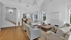 A spacious living room with a staircase, a fireplace, and a large window. - Village Oaks Escape | Home steps to the Village! (St Simons Island)