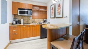 Una cocina compacta con armarios de madera, un microondas, una cafetera y un lavamanos.