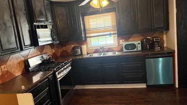 A kitchen with dark cabinets, a stove, a microwave, a coffee maker, and a dishwasher. -     Relax & Unwind Stylish Decatur Home Near Downtown ATL (Decatur)