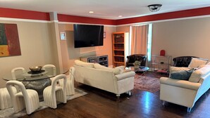 A spacious living room with a wooden floor, white sofas, a glass coffee table, and a flat-screen TV mounted on the wall. -     Relax & Unwind Stylish Decatur Home Near Downtown ATL (Decatur)
