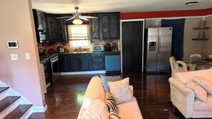 A modern kitchen with dark cabinets, a refrigerator, and a dining area with a white table and chairs. -     Relax & Unwind Stylish Decatur Home Near Downtown ATL (Decatur)