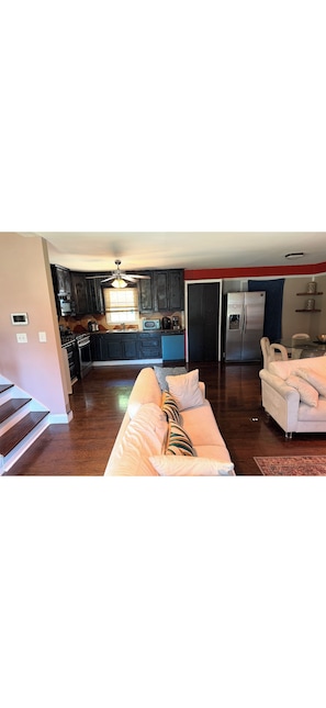 A modern kitchen with dark cabinets, a refrigerator, and a dining area with a white table and chairs. -     Relax & Unwind Stylish Decatur Home Near Downtown ATL (Decatur)