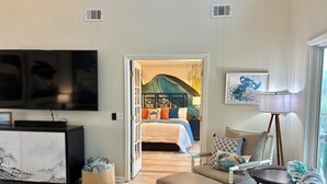 Ein modernes Wohnzimmer mit Flachbildfernseher, einer Couch, einem Couchtisch und einem Bett mit dekorativer Kopfteil.