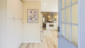 Ein Flur, der zu einer Küche mit modernem Design führt, mit einer Glastür und einem gerahmten Kunstwerk an der Wand.