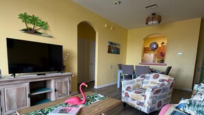 Sala de estar com televisão, móveis de madeira, ventilador de teto e área de jantar com cadeiras.