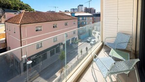 A balcony with a glass railing, two patterned chairs, and a view of buildings and a hill. - Dream retreat pool and gym (Gibraltar)