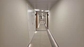 A long, narrow hotel corridor with doors on both sides and a tiled floor.