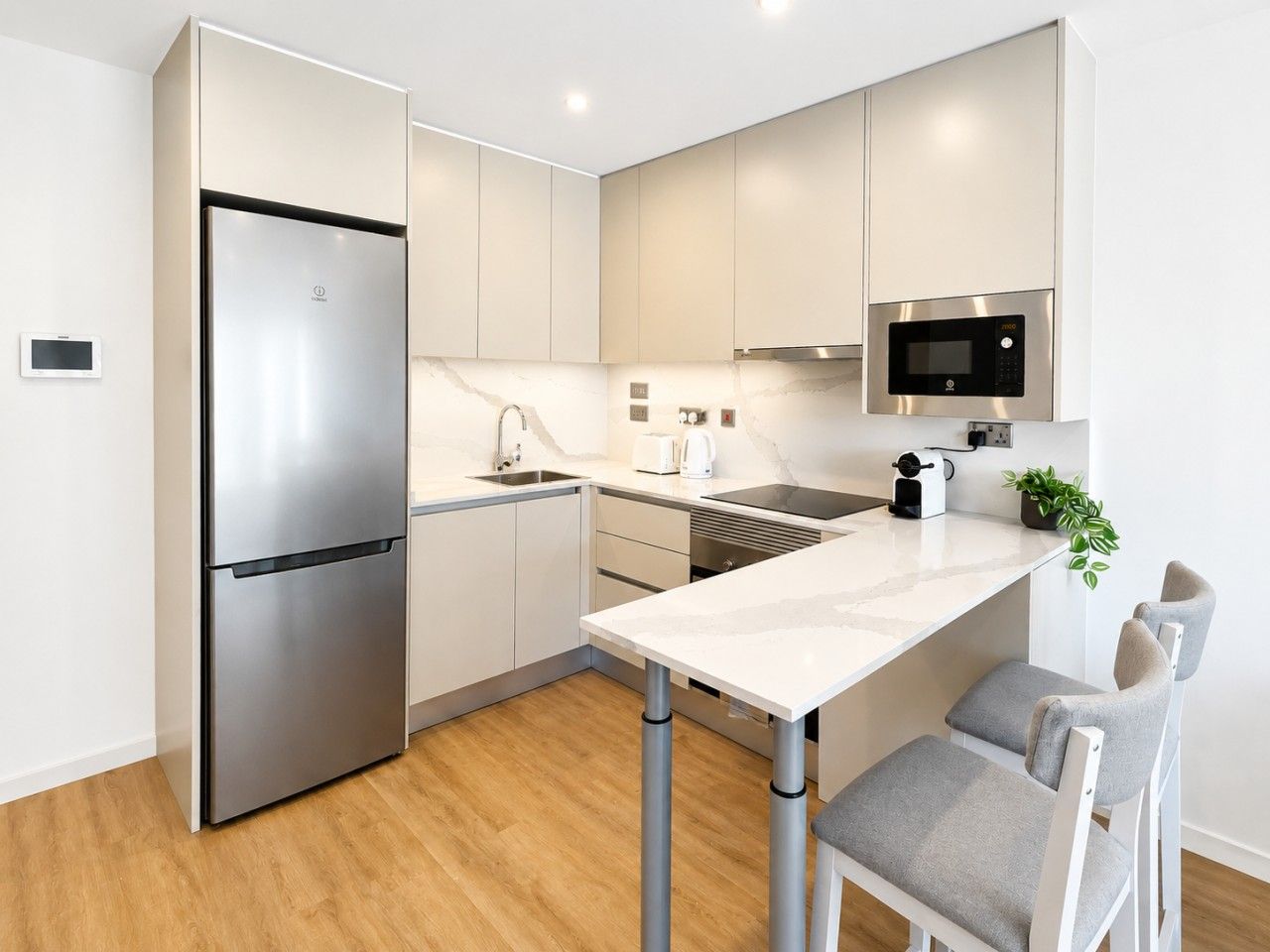 Una cocina moderna con un refrigerador de acero inoxidable, un microondas, un lavamanos y un comedor con sillas.