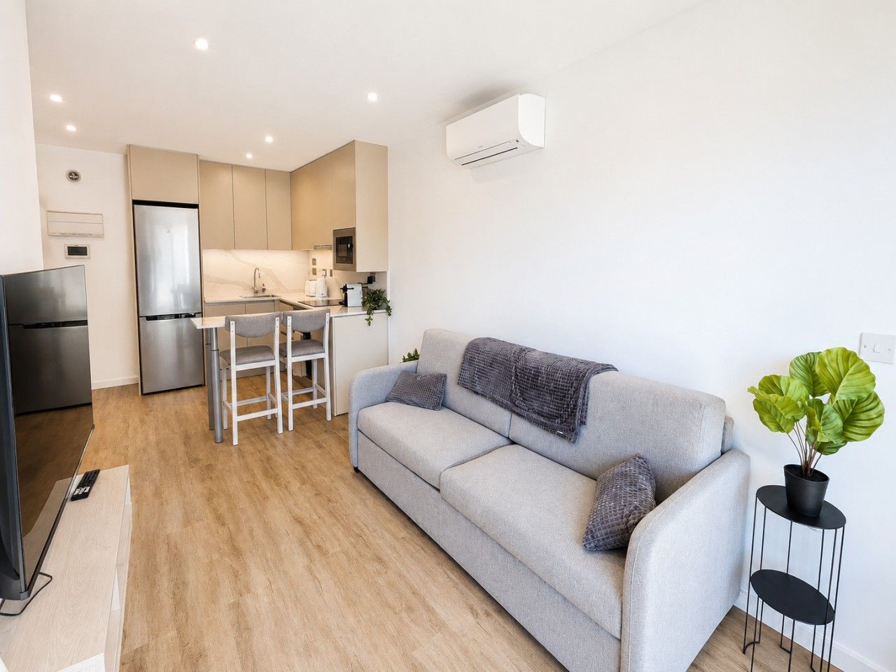 Een moderne woonkamer met een bank, een eettafel en een keuken met een koelkast en magnetron.
