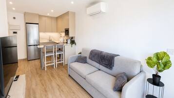 Una sala de estar moderna con un sofá, una mesa de comedor y una zona de cocina con refrigerador y microondas.