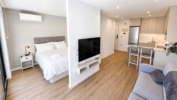 A modern hotel room with a bed, TV, kitchenette, and a sofa. - Dream retreat pool and gym (Gibraltar)