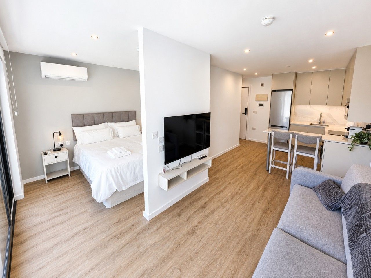 Een moderne hotelkamer met een bed, televisie, kitchenette en een bank.
