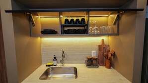 A kitchen with a stainless steel sink, a built-in shelf with black bowls and wine glasses, and wooden utensils on the countertop.