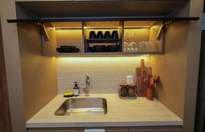Eine Küche mit einer Spüle aus Edelstahl, einem eingebauten Regal mit schwarzen Schüsseln und Weingläsern sowie Holzkocherutensilien auf der Arbeitsfläche.