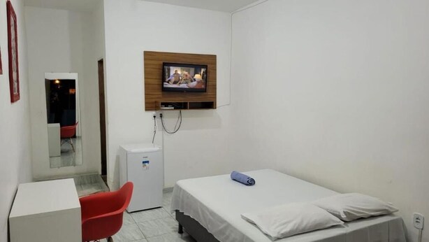 A small, clean room with a bed, a desk, a chair, a TV mounted on the wall, and a small refrigerator. - Center Hotel Picos (Picos)