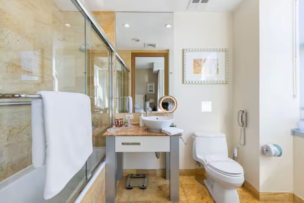 Ein Badezimmer mit Duschkabine aus Glas, Waschbecken mit Waschtisch, Toilette und einem gerahmten Bild an der Wand.