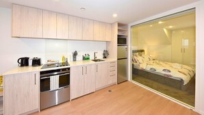 A modern kitchen with a dishwasher, oven, and microwave. There is a sliding glass door leading to a bedroom with a bed. - Modern One Bedroom Stay on Bath Street (Christchurch)