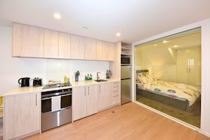 Eine moderne Küche mit Geschirrspüler, Backofen und Mikrowelle. Eine Schiebetür führt zu einem Schlafzimmer mit einem Bett.