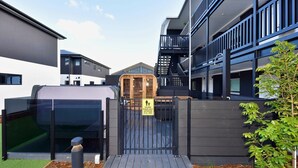 A gated entrance to a modern building with a wooden door, a sign indicating a child-friendly area, and a small garden area with mulch and a tree. - Modern One Bedroom Stay on Bath Street (Christchurch)