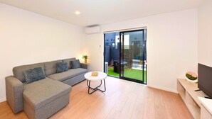 A modern living room with a grey sofa, a small white table, and a TV on a stand. - Modern One Bedroom Stay on Bath Street (Christchurch)