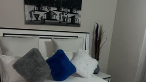Un lit avec un matelas blanc, un coussin bleu et un coussin gris, un oreiller blanc et une couverture bleu clair.