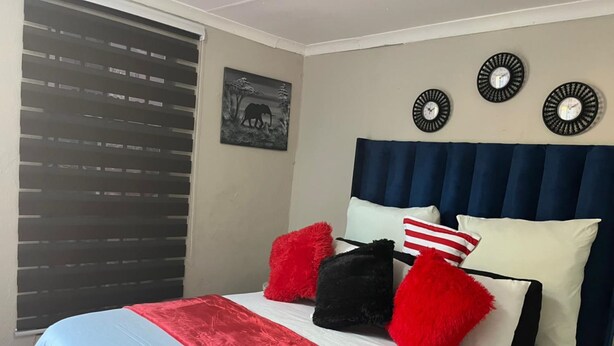 Une chambre à coucher avec un lit, une fenêtre avec des stores, une horloge murale et un tableau encadré.