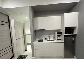 A compact kitchen with white cabinets, a black countertop, a stainless steel sink, a microwave, and a refrigerator. - Studio Suites Near PWTC Kuala Lumpur,Malaysia (Wilayah Persekutuan)