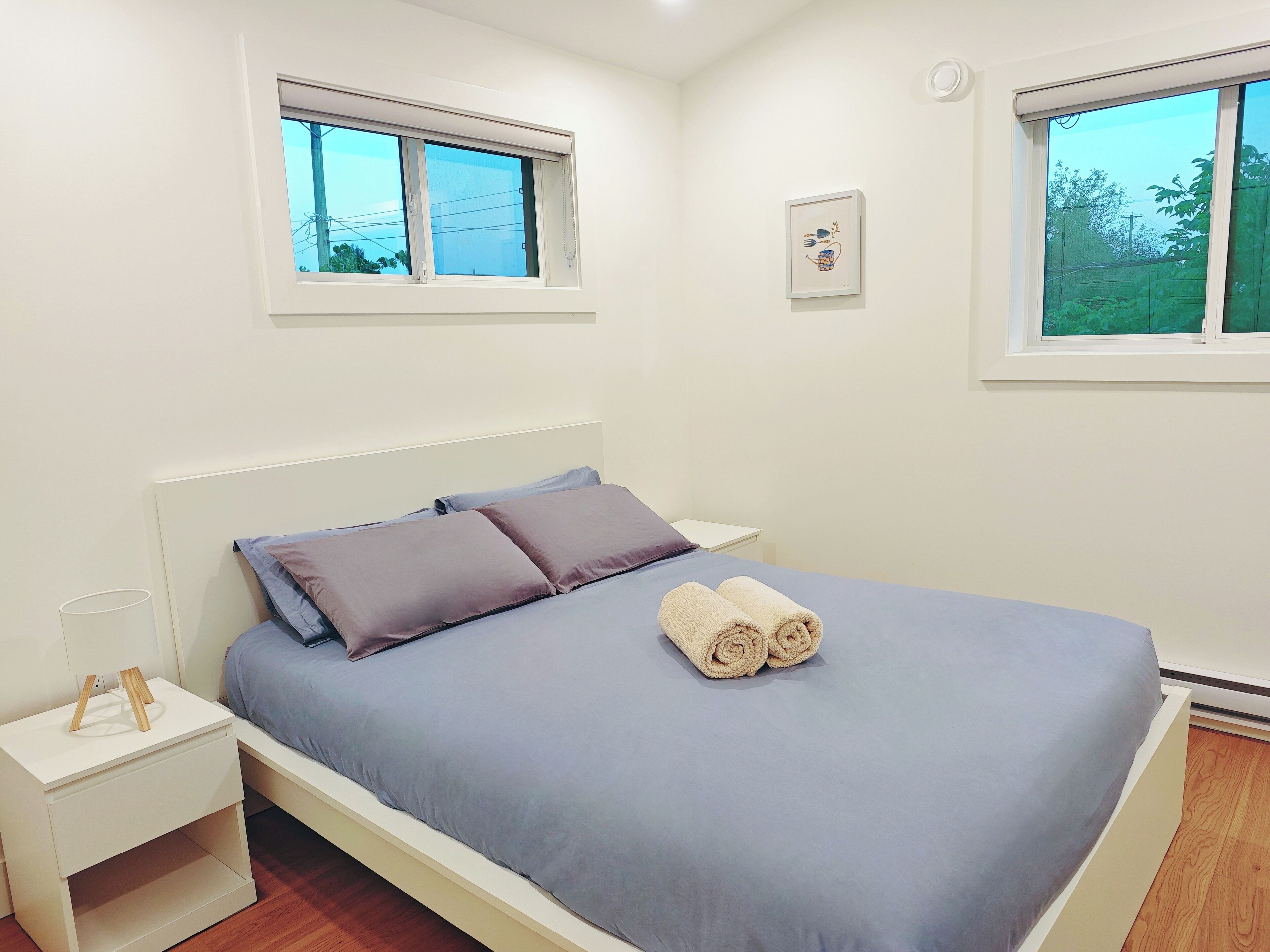 A bedroom with a bed, two nightstands, a window, and a wall-mounted picture.