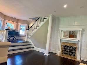 A staircase with dark wood steps and white railings, leading to a room with a fireplace and a window with a view. - Distinctive 4-Bed 4.5 Bath Victorian Home in Beautiful Summit NJ. Fully Updated. (Summit)