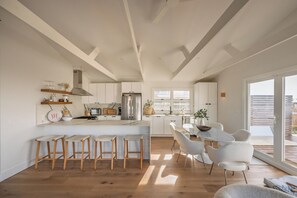 A modern kitchen with a central island, bar stools, and a dining area with white chairs.