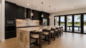 A modern kitchen with a marble island, built-in ovens, pendant lighting, and a view of a pool. - Luxury Miami 5BR Retreat W/Pool,Jacuzzi & Outdoor Kitchen . (Miami)