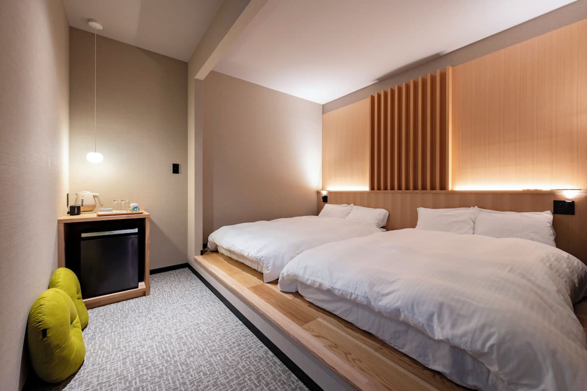 Hotellihuone, jossa on sänky, yöpöydät, lamppu ja seinälle asennettu paneeli.