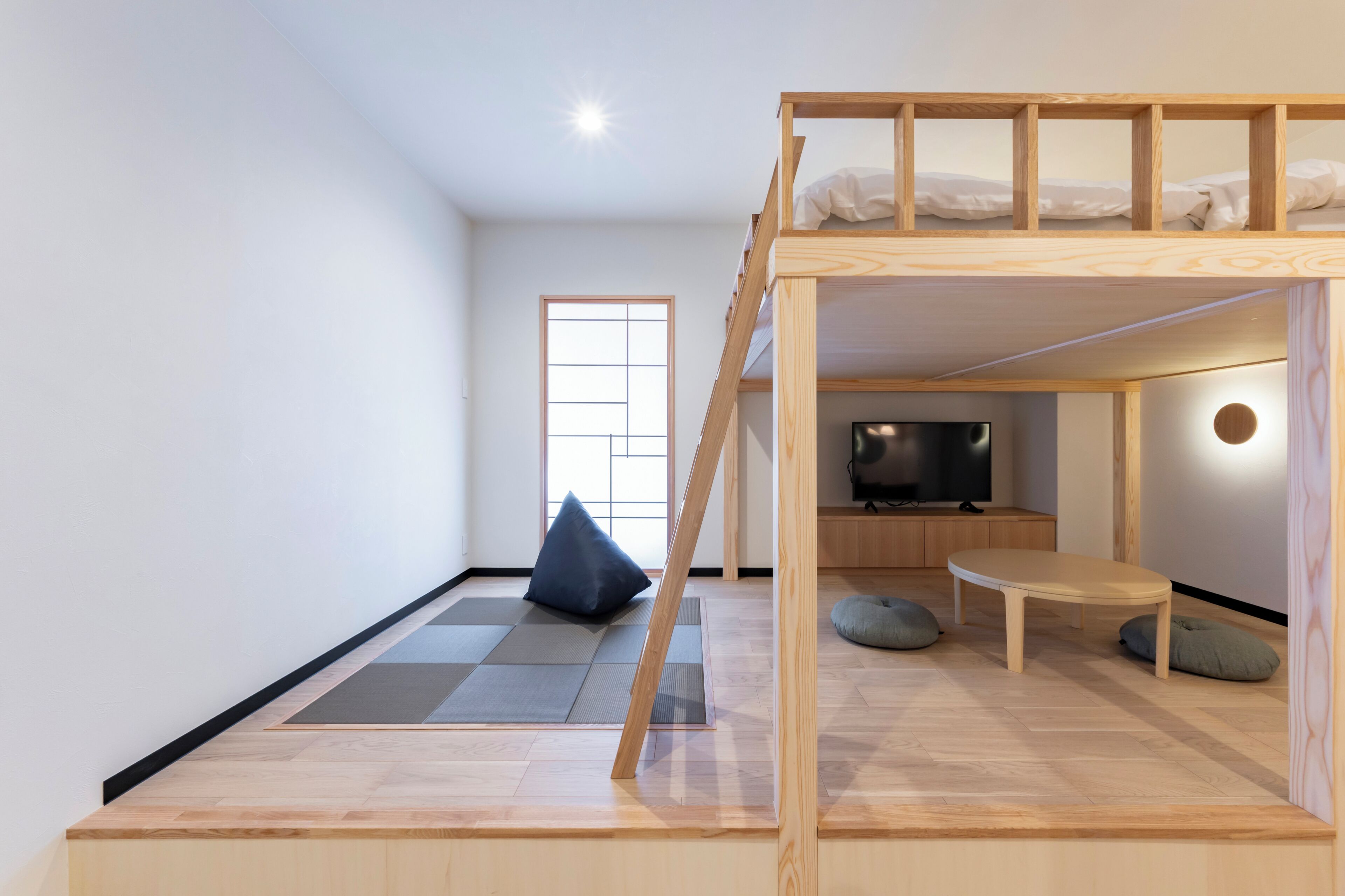 A room with a bunk bed, tatami mat flooring, a television, and a small table.