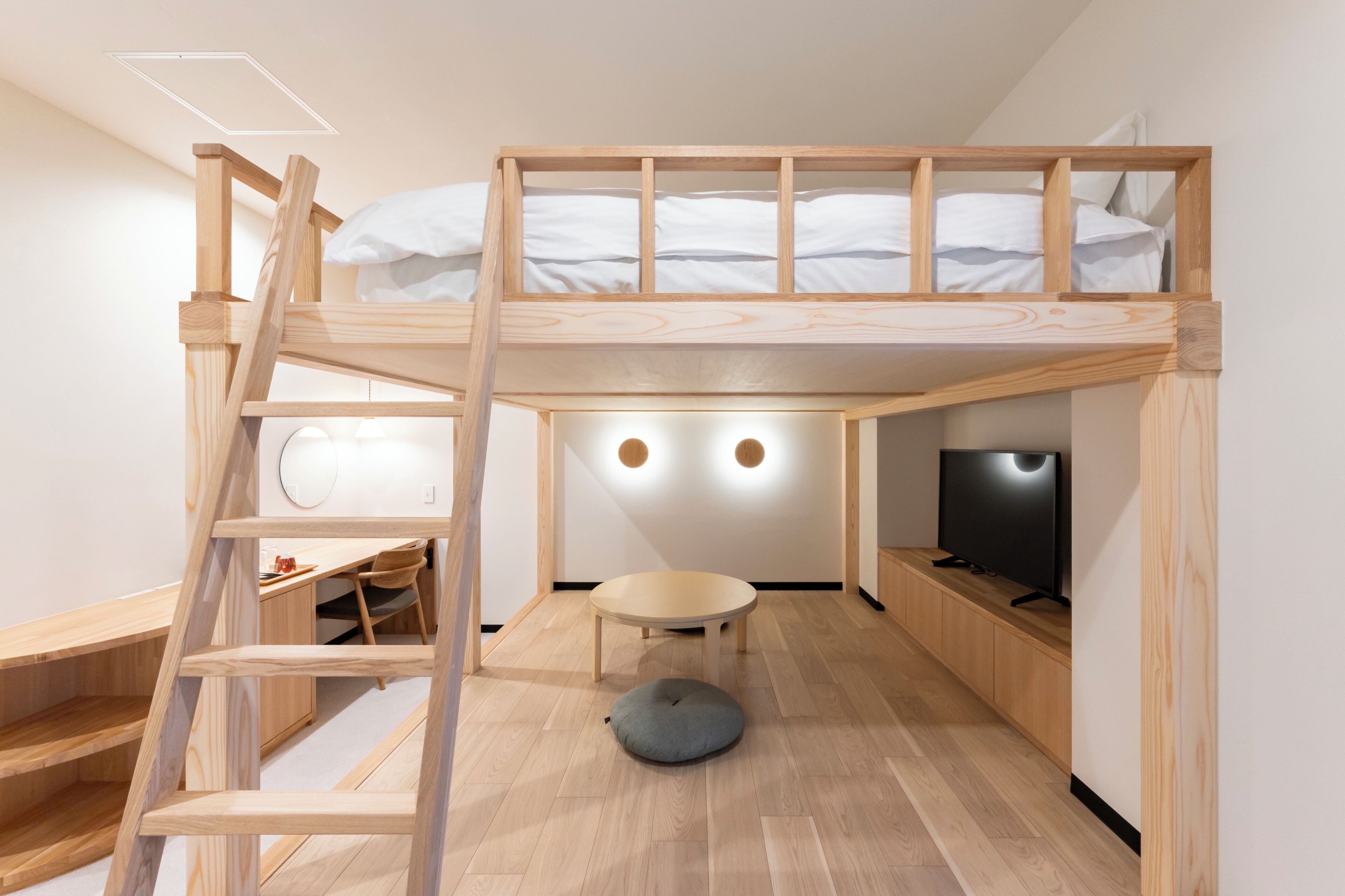A bunk bed with a desk and chair, a round table, and a television.