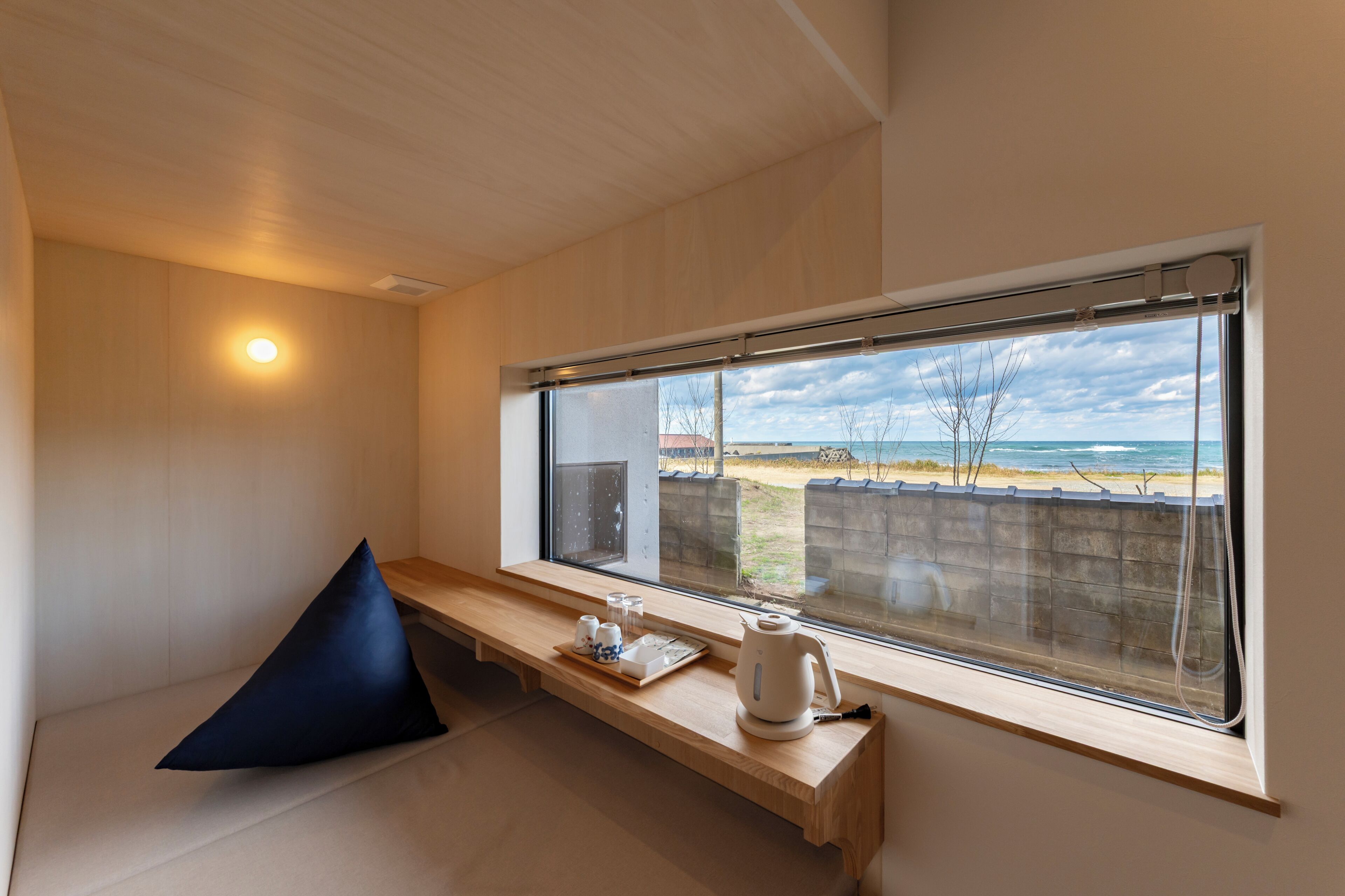A room with a large window, a bench, a pillow, and a tray with cups and a kettle.