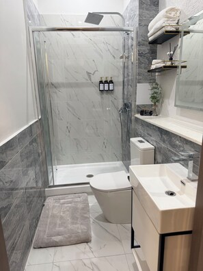 Un baño moderno con ducha envuelta en vidrio, inodoro, lavamanos y azulejos de mármol.