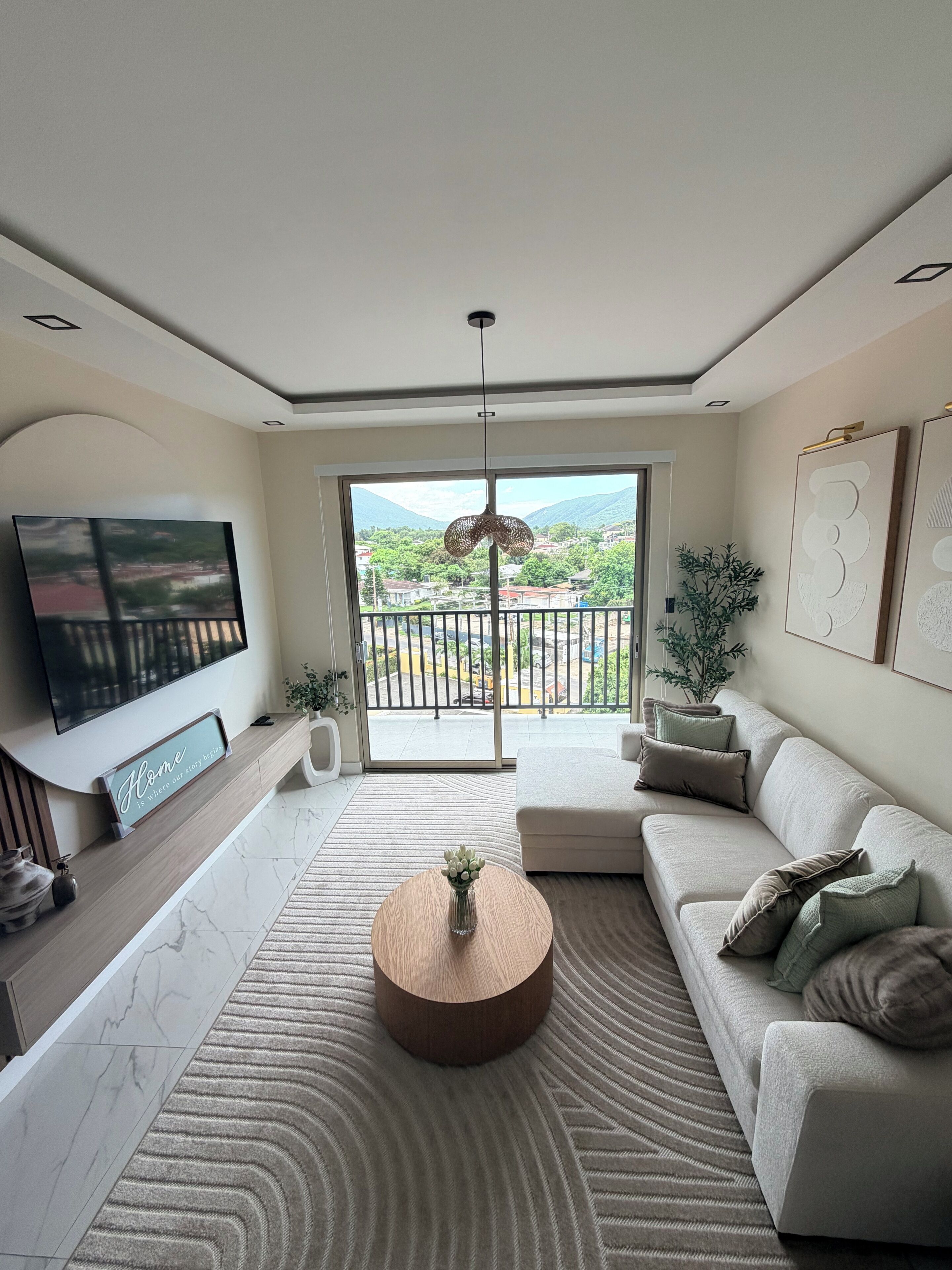 A modern living room with a large TV, a sofa, a coffee table, and a view of a balcony.