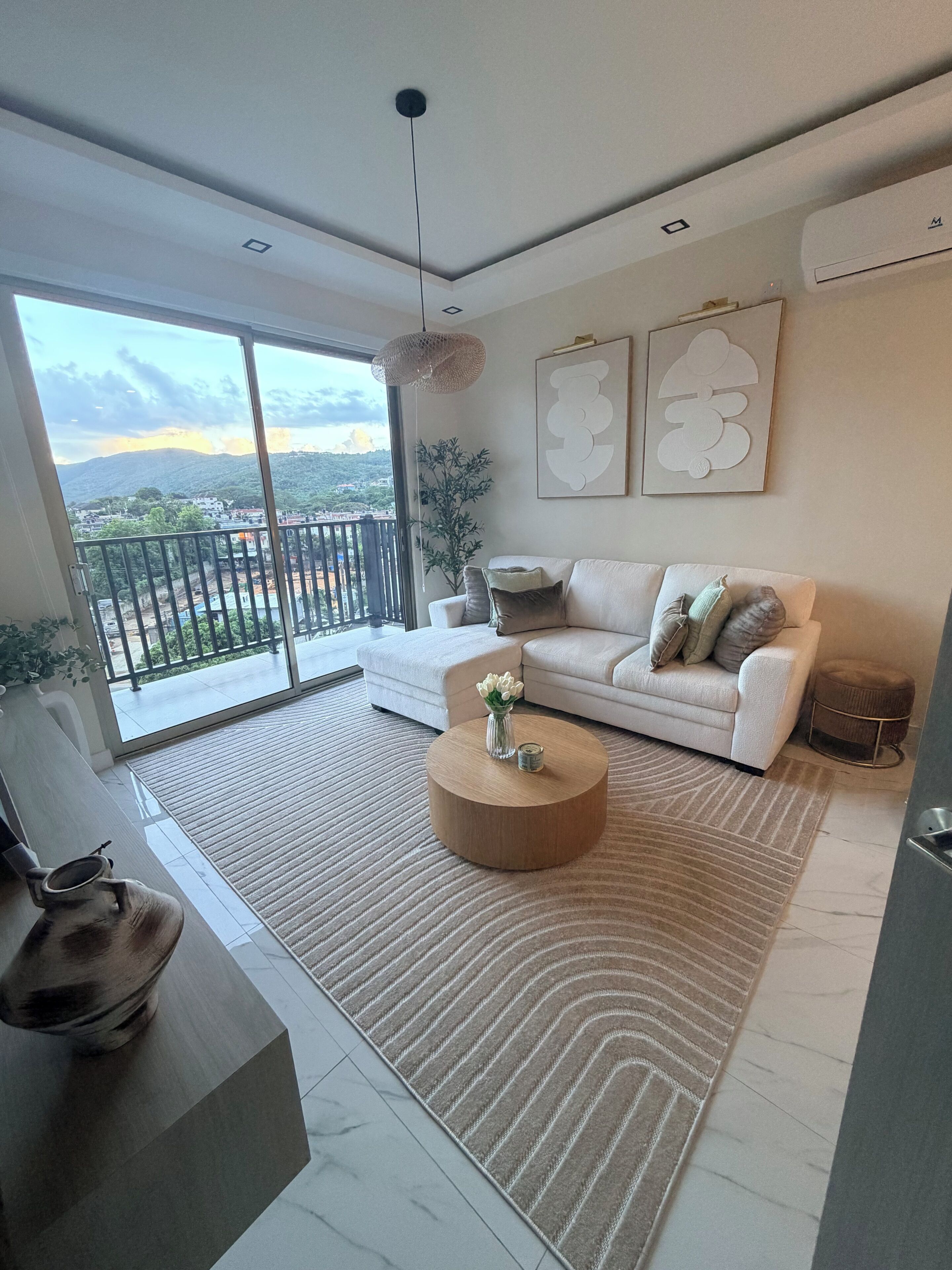 A modern living room with a sofa, a coffee table, and a view of a mountainous landscape through large windows.
