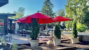 Un patio al aire libre con sombrillas rojas, plantas en macetas y un área de asientos de piedra.