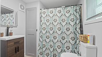 Een badkamer met een witte wastafel, houten kastje, toilet en douchegordijn met dessin.