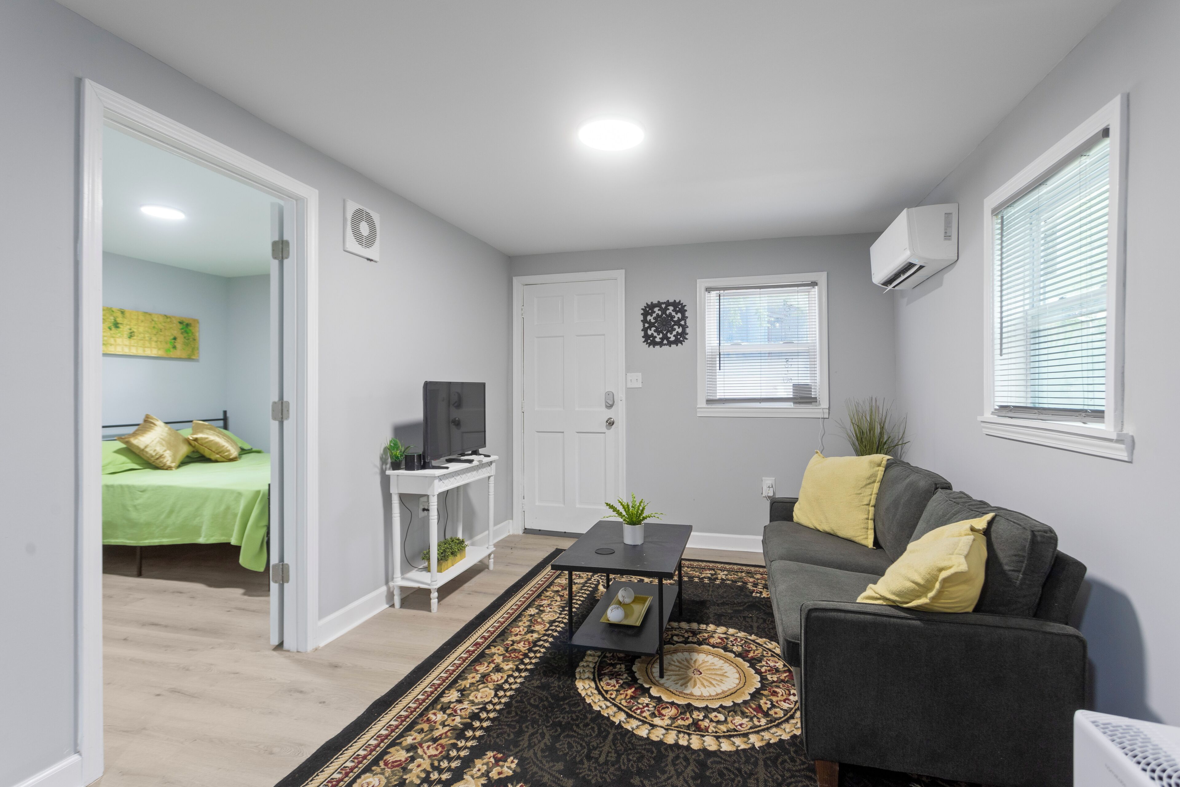 Een woonkamer met een bank, salontafel, televisie en een deur naar een slaapkamer.