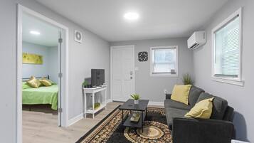Een woonkamer met een bank, salontafel, televisie en een deur naar een slaapkamer.