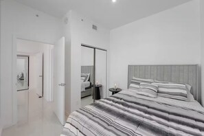 Ein Schlafzimmer mit einem großen Bett, einem Kleiderschrank, einem Nachttisch mit Lampe und einem Spiegel.