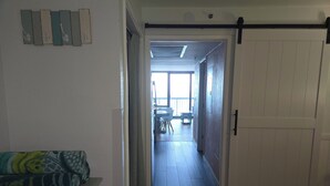 A hallway leading to a balcony with a dining area, a white door, and a patterned sofa. - Oceanfront Nautical Escape. Pools, Lazy River & Stunning Views (Myrtle Beach)
