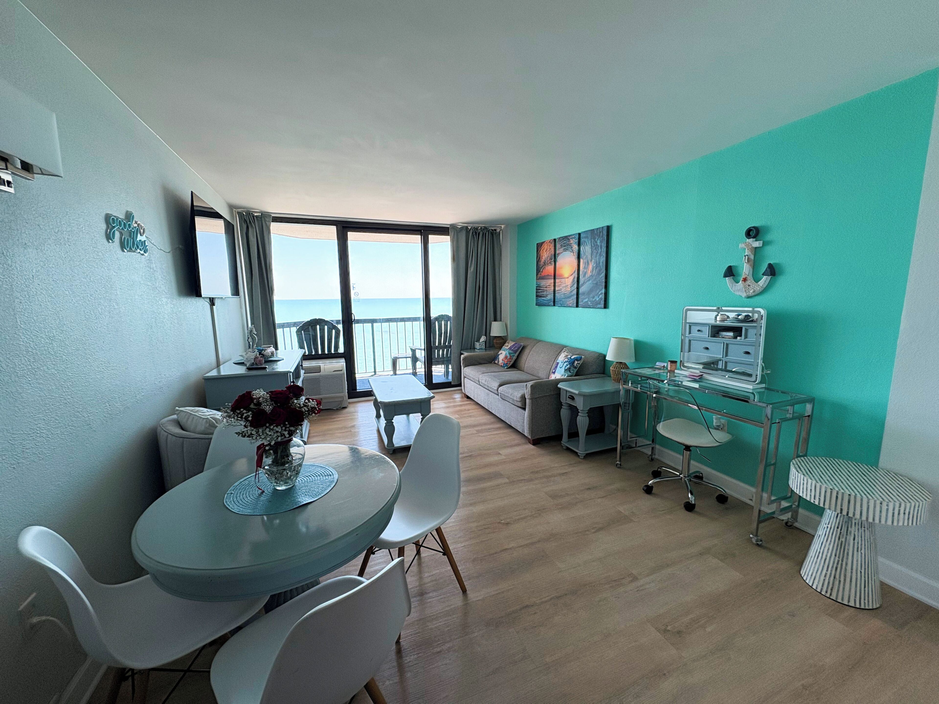 Un salon moderne comprenant un coin repas, un ensemble de canapés, une table en verre et une vue sur la mer grâce à de grandes fenêtres.