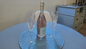 A table with a bottle of Prosecco and two glasses on a woven placemat, a neon sign, and a TV on the wall. - Oceanfront Nautical Escape. Pools, Lazy River & Stunning Views (Myrtle Beach)
