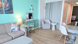 A living room with a sofa, a small table, a desk with a computer, a chair, and a dining table with chairs. - Oceanfront Nautical Escape. Pools, Lazy River & Stunning Views (Myrtle Beach)