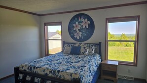 Ein Schlafzimmer mit Bett, zwei Fenstern, einem Nachttisch und einem Wandbild.
