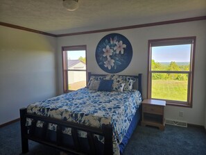 Ein Schlafzimmer mit Bett, zwei Fenstern, einem Nachttisch und einem Wandbild.